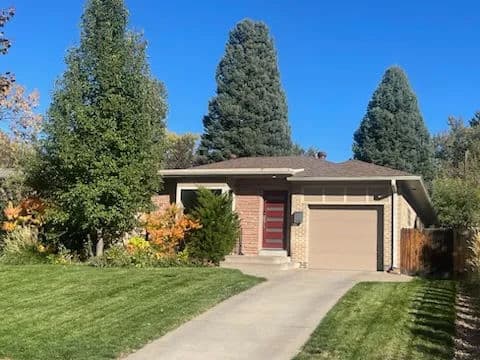 Charming suburban home with landscaped lawn and tall trees under a clear blue sky.